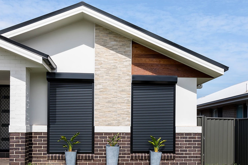 Charcoal roller shutters on the windows of a brick home