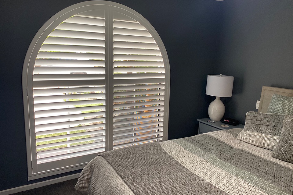 White arched plantation shutters on a bedroom window