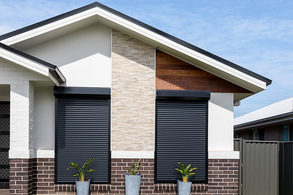 Charcoal roller shutters on two windows of a modern home with a stone feature wall