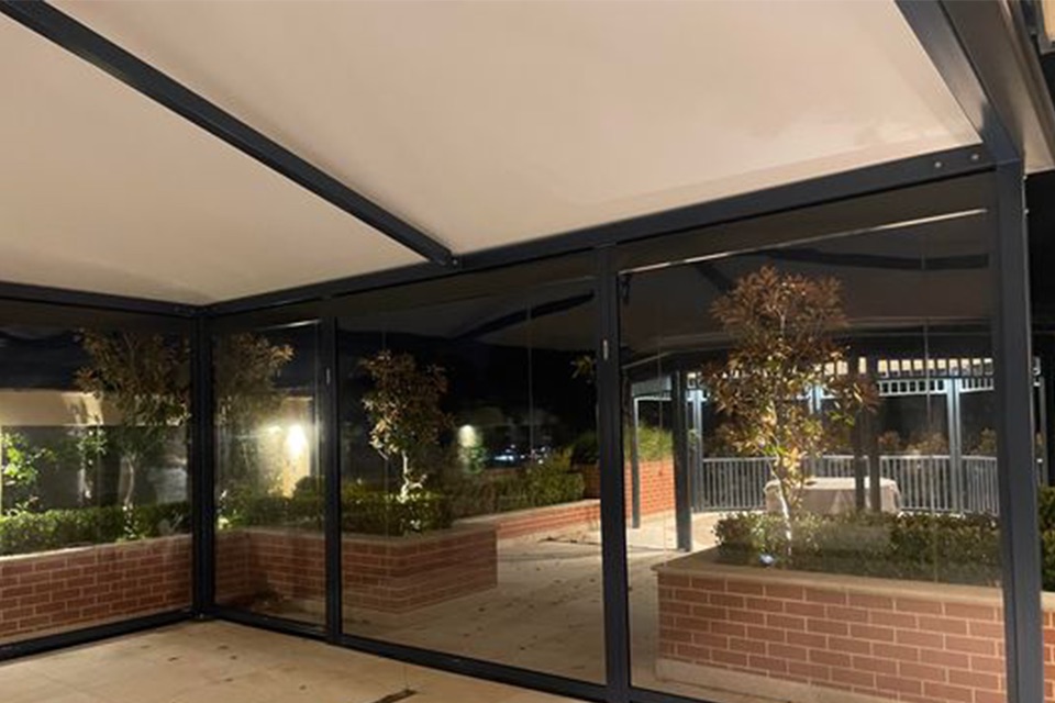 Clear PVC cafe blinds enclosing a lit courtyard dining area with planter boxes at night