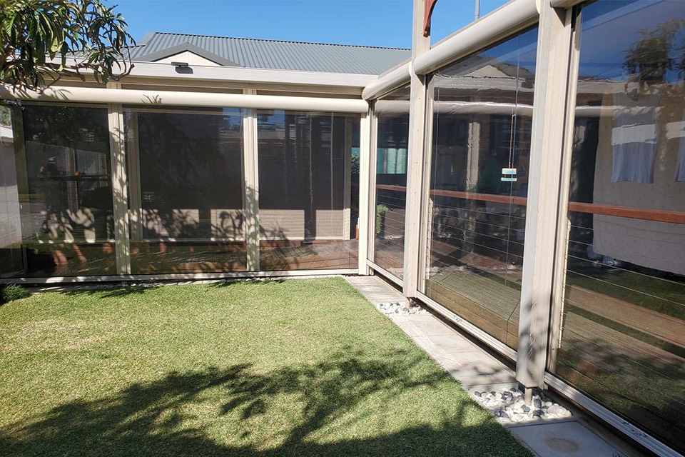 Clear PVC cafe blinds on a cream-framed patio facing a lawn