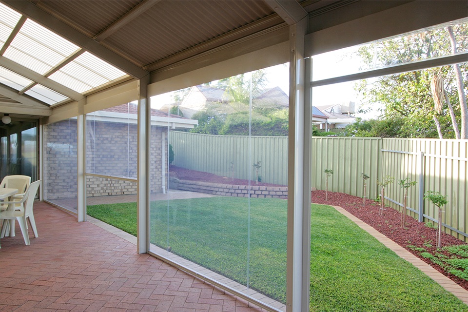 Clear PVC cafe blinds enclosing a home patio with paved floor, looking out to a lawn
