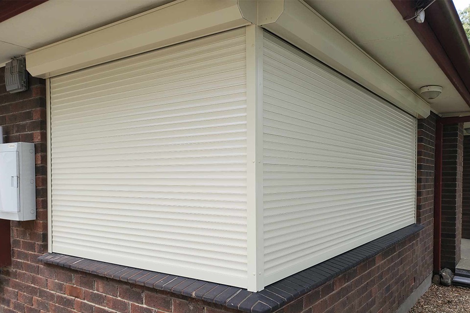 Cream roller shutter on a wide window under the eaves of a brick home