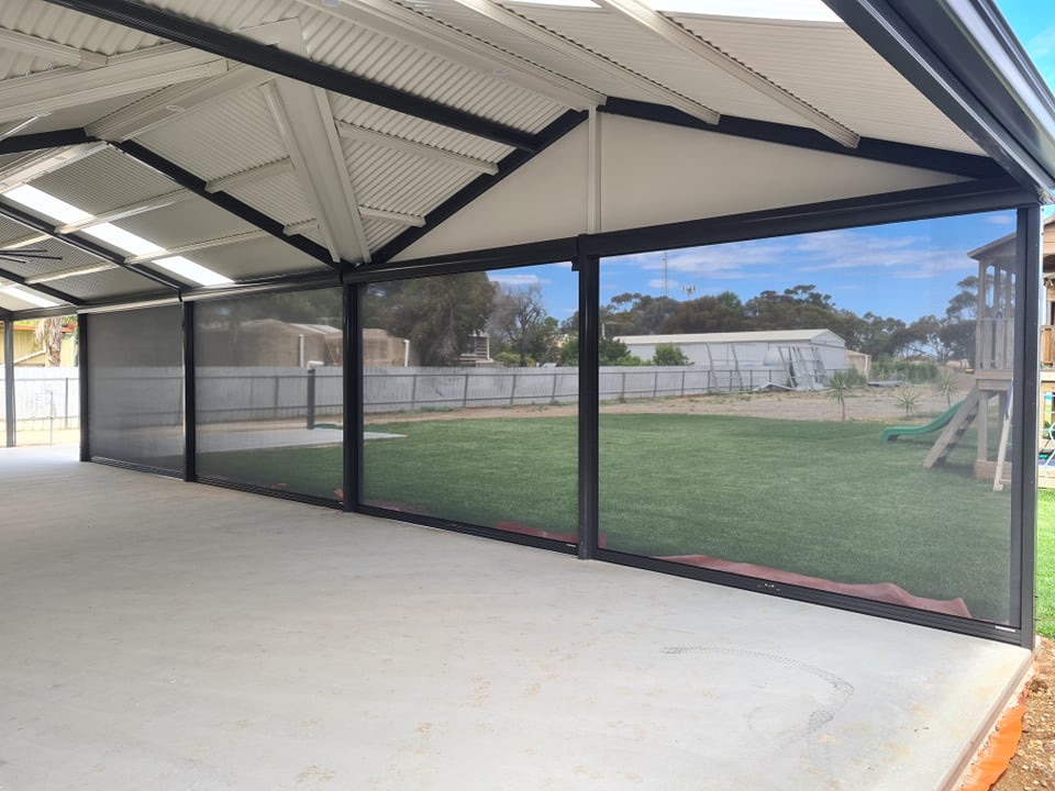 Gable patio with roof lights and outdoor blinds lowered around a concrete slab