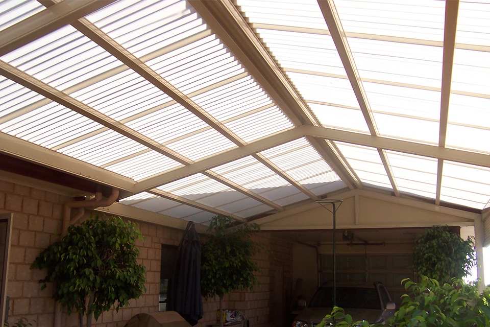Gable pergola with a translucent polycarbonate roof over a courtyard beside a brick home