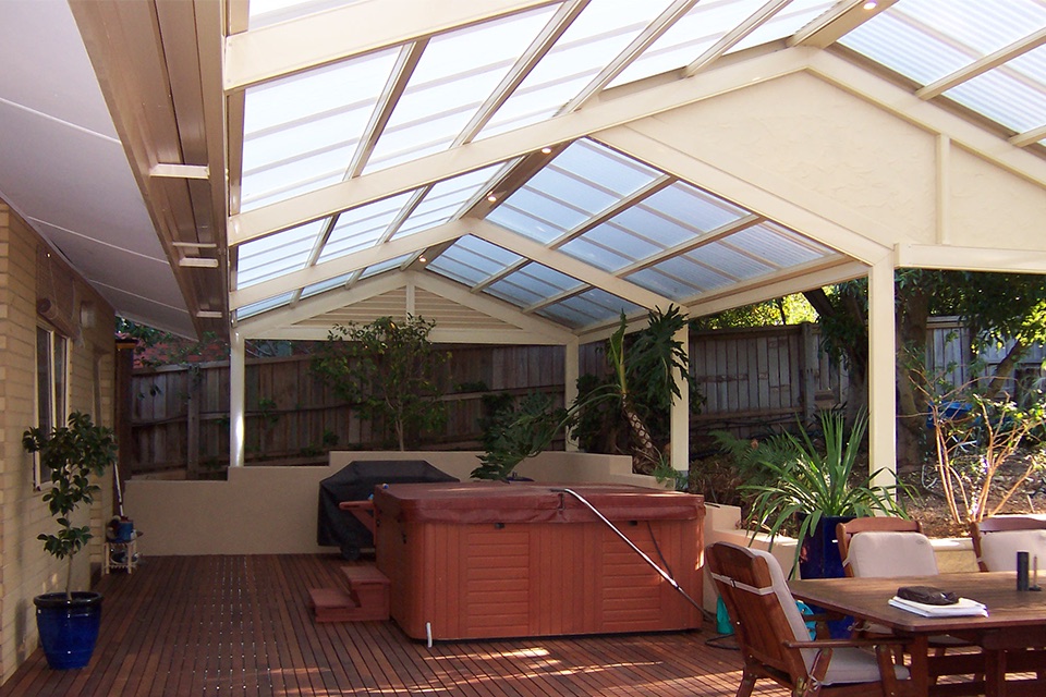 Gable pergola with a polycarbonate roof over a timber deck with a spa and outdoor dining
