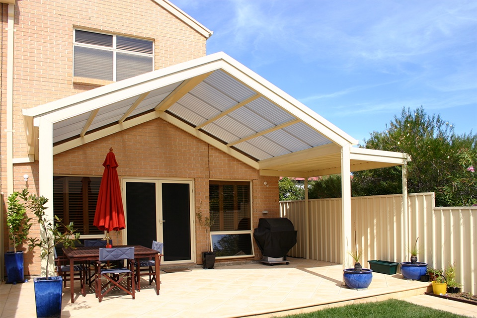 Cream gable pergola with a polycarbonate roof over a paved dining area of a two-storey home