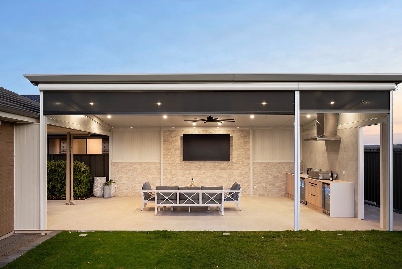 Large insulated patio with downlights, a ceiling fan, outdoor blinds, a TV wall and an outdoor kitchen over a tiled floor