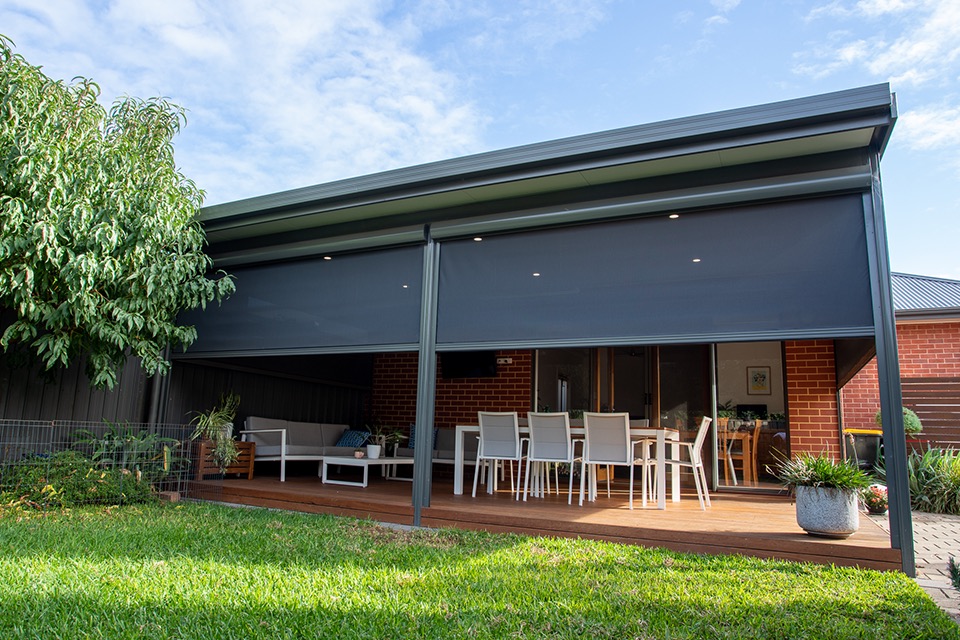 Outdoor blinds partly raised on a skillion patio over a timber deck with outdoor dining and lounge furniture