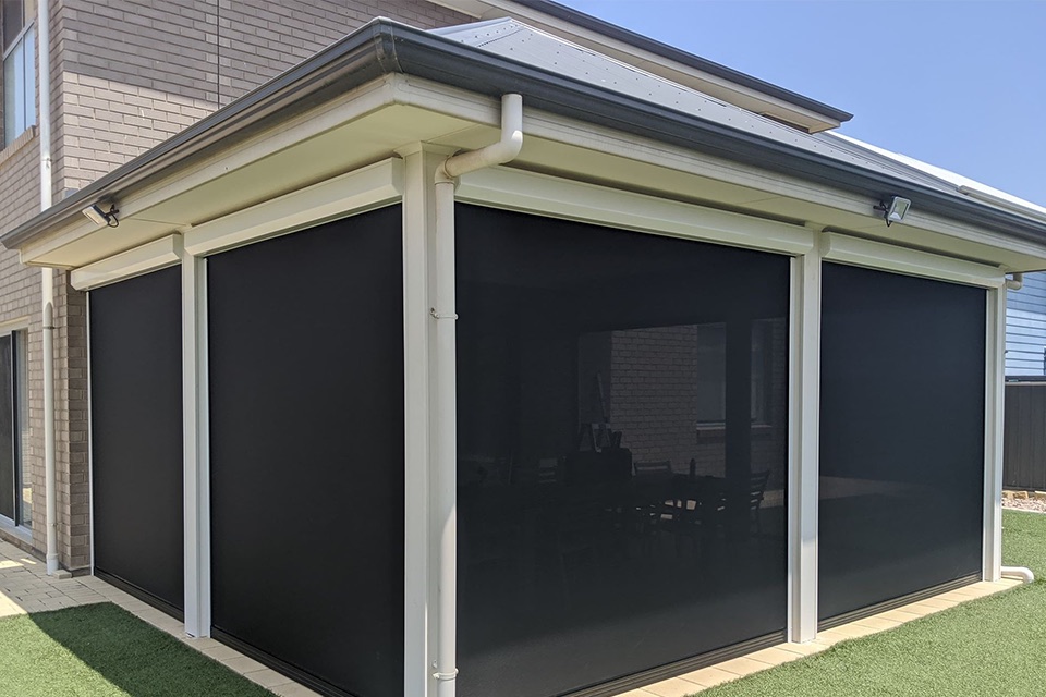 Dark mesh outdoor blinds on a white-framed corner patio of a two-storey home