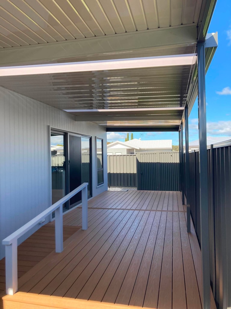 Flat patio roof over a composite deck with a white handrail beside a weatherboard home