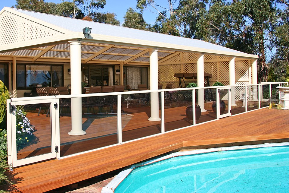 Timber pool deck with a glass and white-framed balustrade beside an above-ground pool