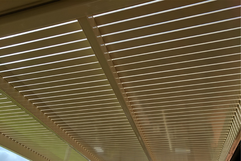 Underside of a steel pergola roof with a cream ribbed ceiling