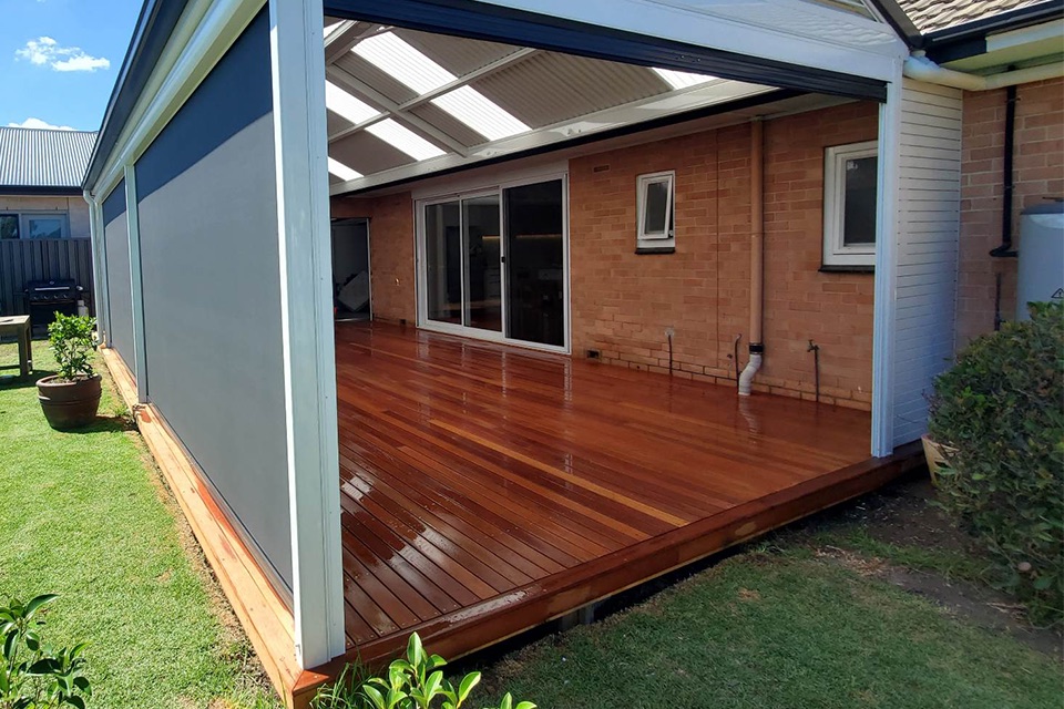 Timber deck along the side of a brick home, partly covered by a patio roof